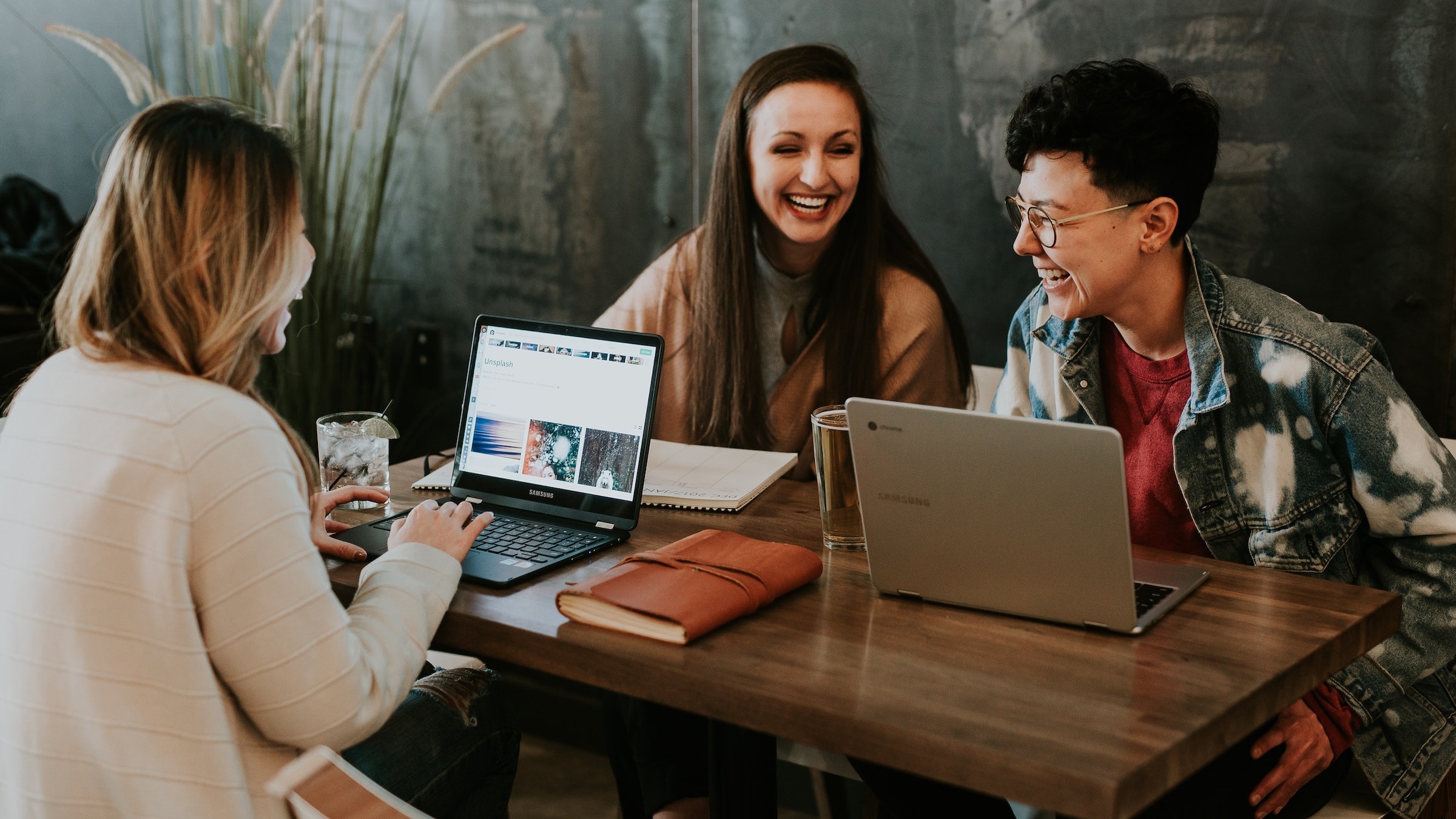 Three staffs of our studio sitting in front of a table, working and laughing, serving as the main image of the about page.